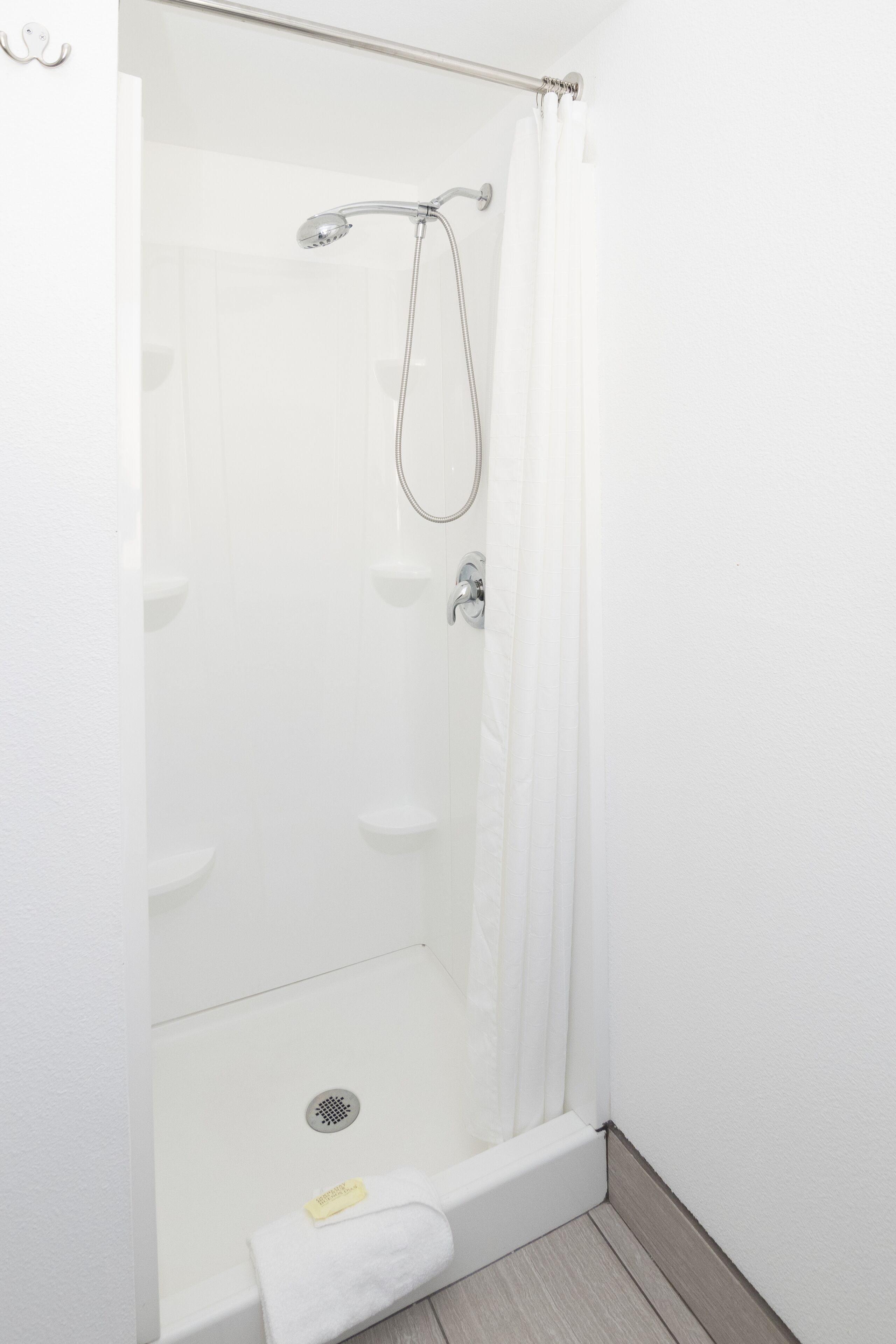 A modern shower with a glass door, a handheld showerhead, and a white towel on the floor.