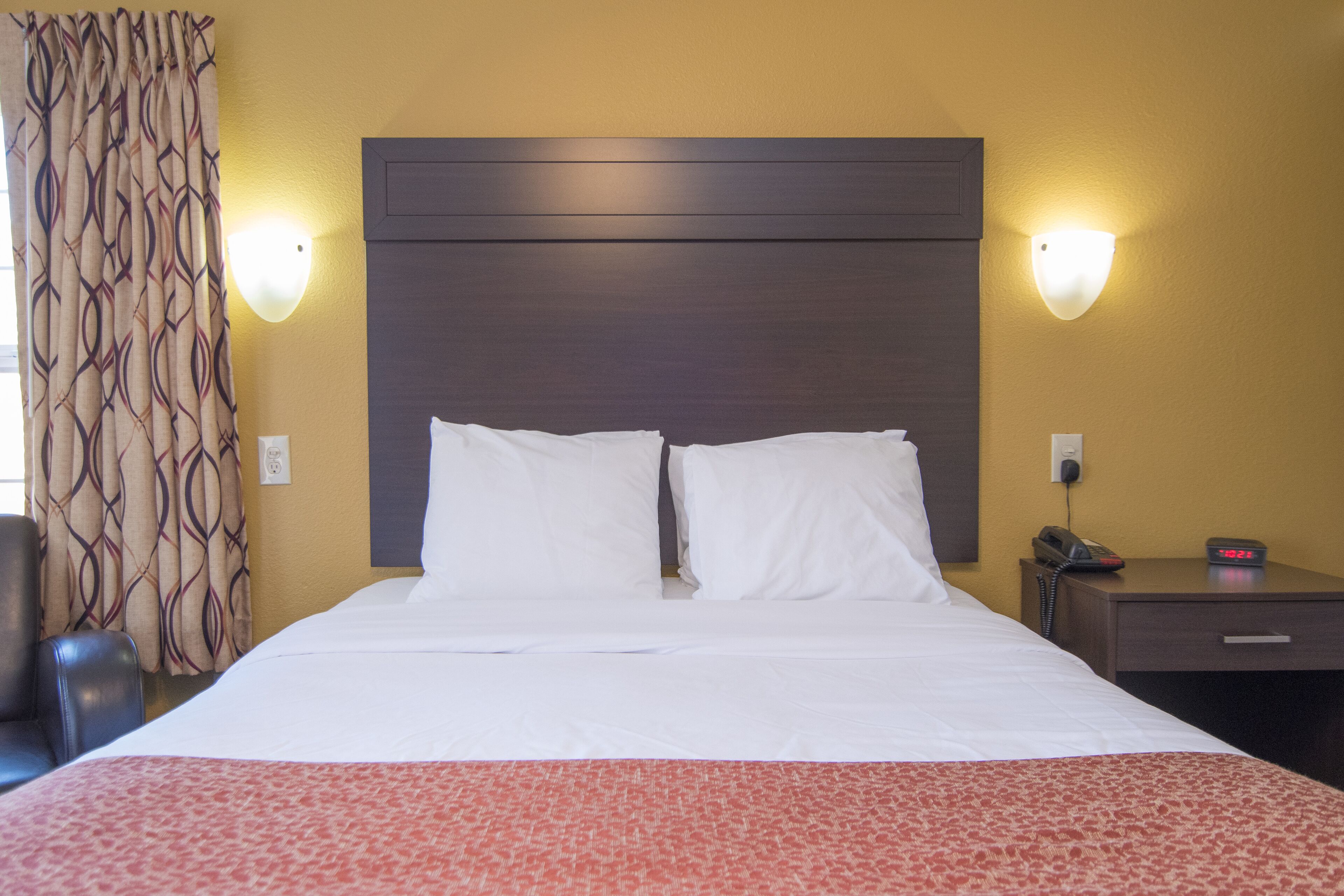 A hotel room with a large bed, two bedside lamps, a nightstand with a phone, and a patterned curtain.
