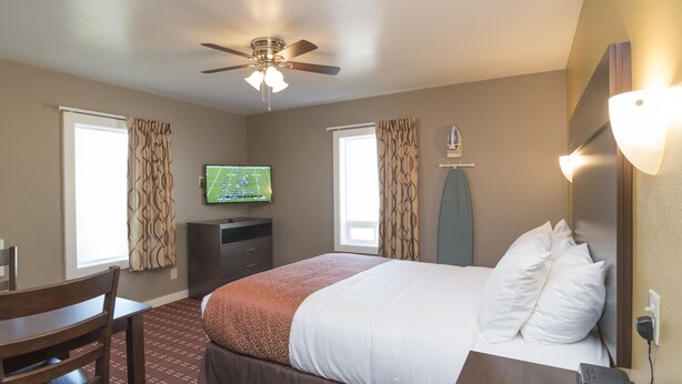 A hotel room with a bed, a desk, a chair, a television, and a ceiling fan. - Capitol Hill Motel (Portland)