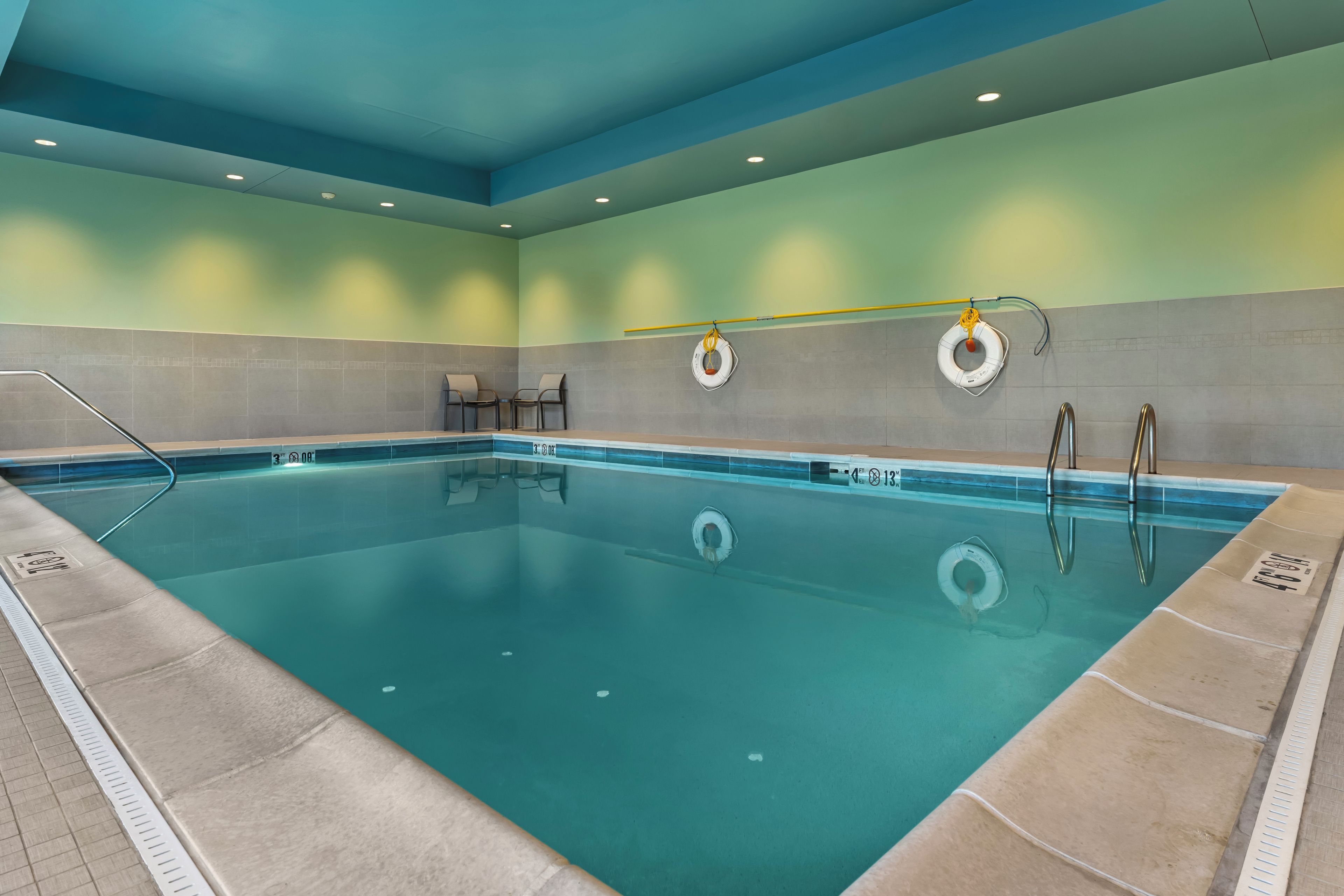 An indoor swimming pool with clear water, marked depth lines, and safety equipment like life rings.