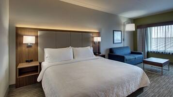 A hotel room with a large bed, bedside tables, a desk, a chair, and a window with curtains.