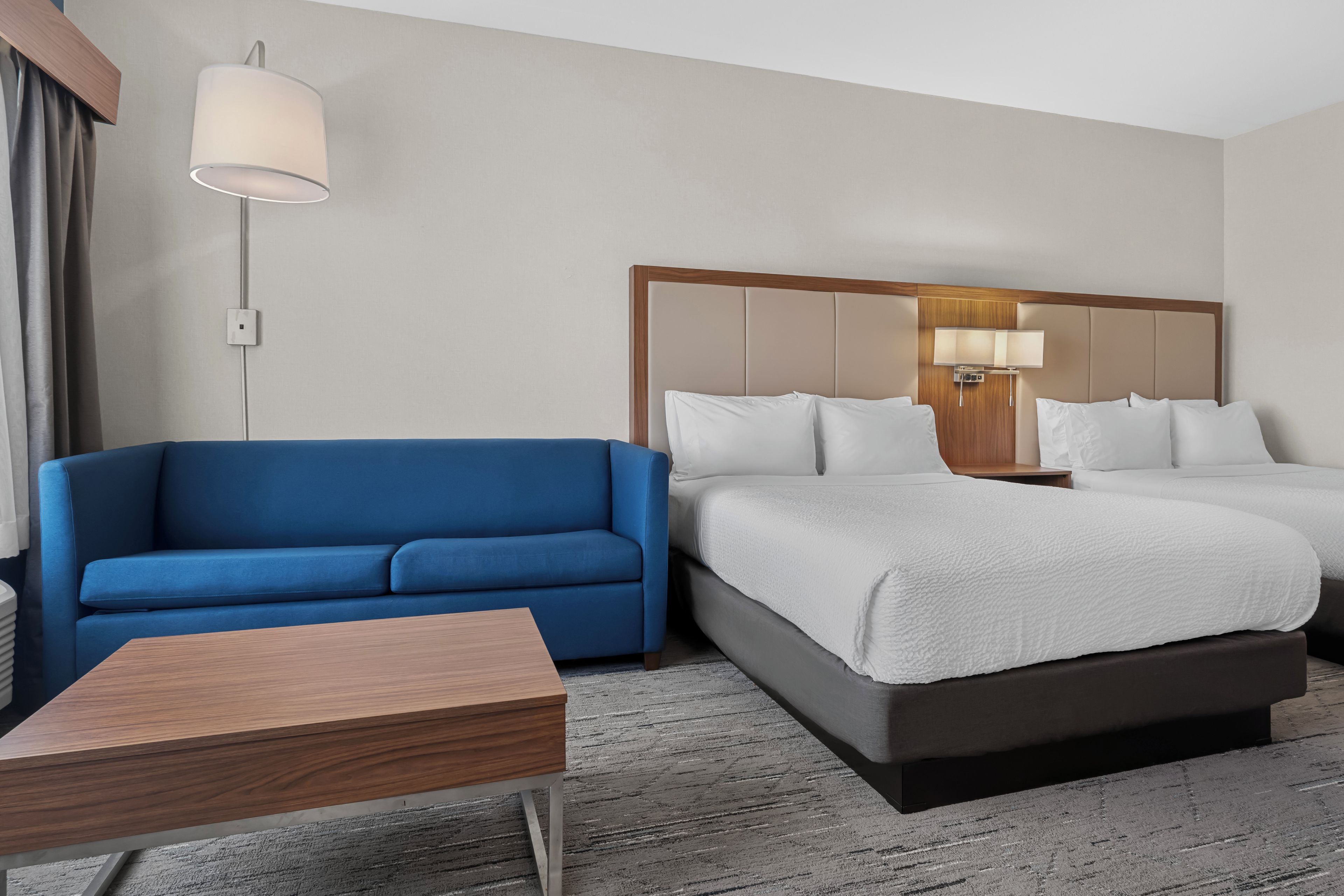 A hotel room with a bed, a blue sofa, a wooden side table, and a lamp.