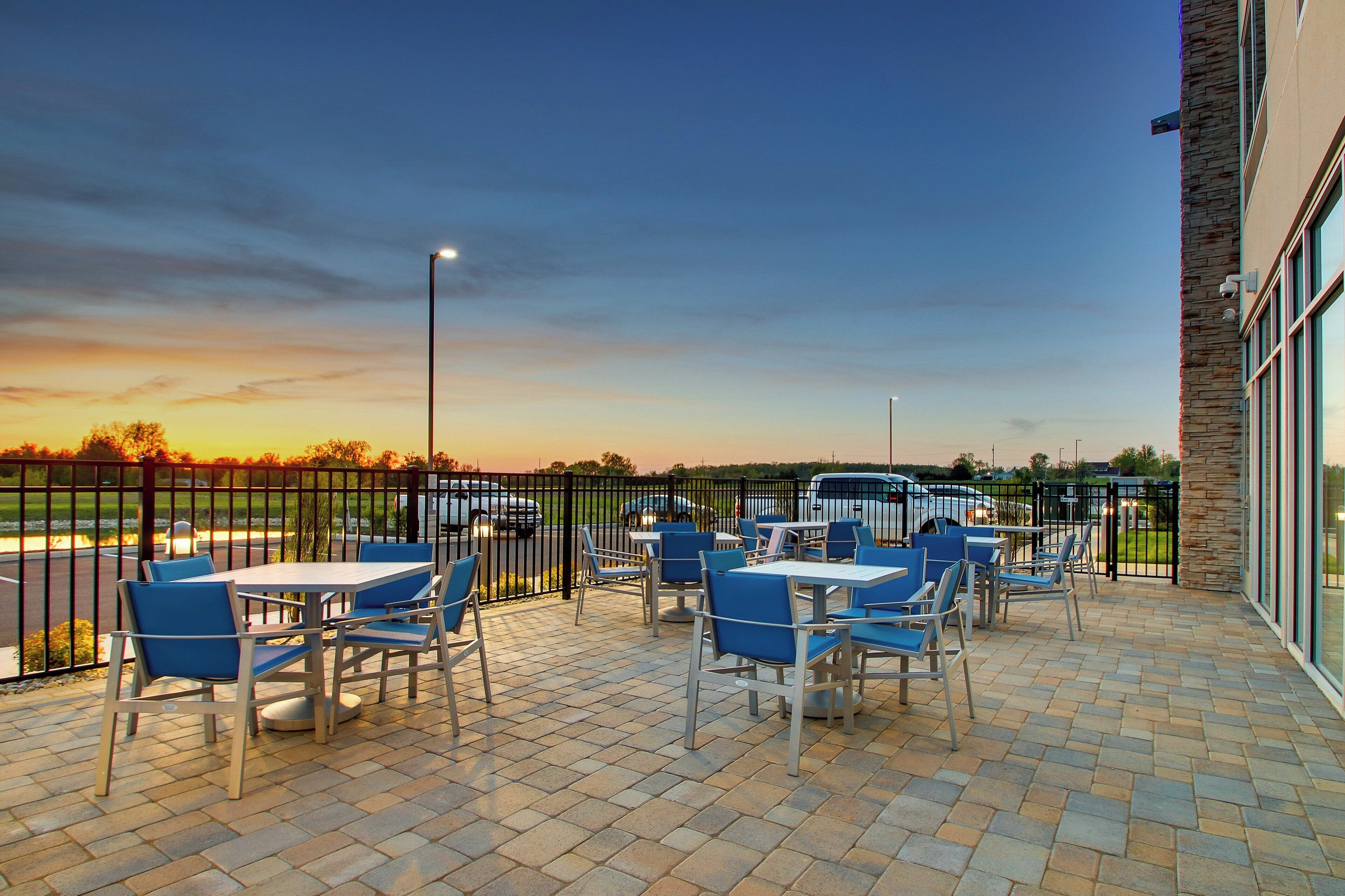 An outdoor patio with tables and chairs, a view of a parking lot, and a building with stone facade.