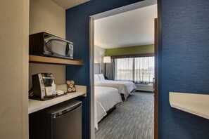 A hotel room with a microwave, coffee maker, and a mini-fridge on a counter. There are two beds with white linens and a window with curtains.