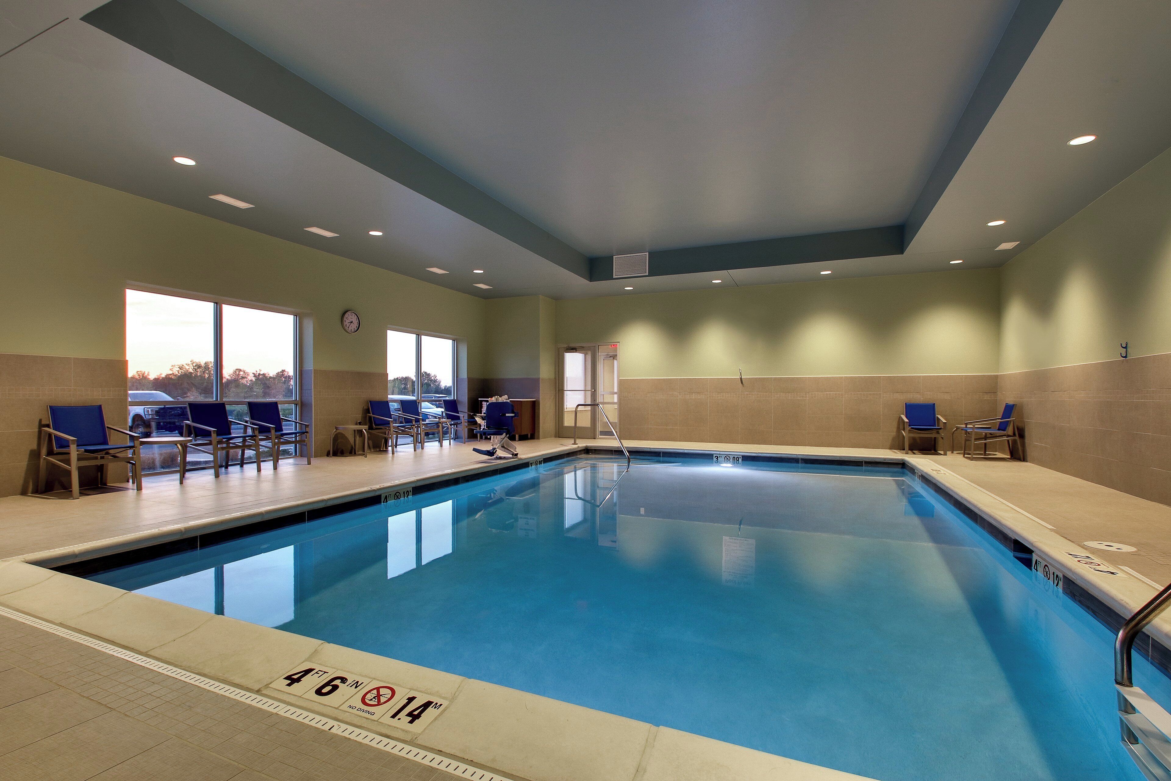 An indoor swimming pool with clear lane markings, a clock on the wall, and seating areas with chairs.