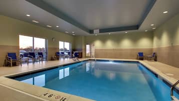 An indoor swimming pool with clear lane markings, a clock on the wall, and seating areas with chairs.