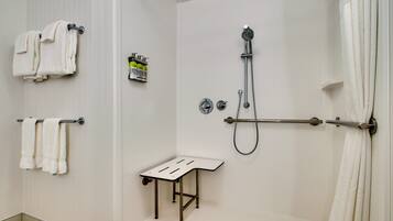 A shower area with a handheld showerhead, a towel rack with folded towels, a small table, and a shower curtain.