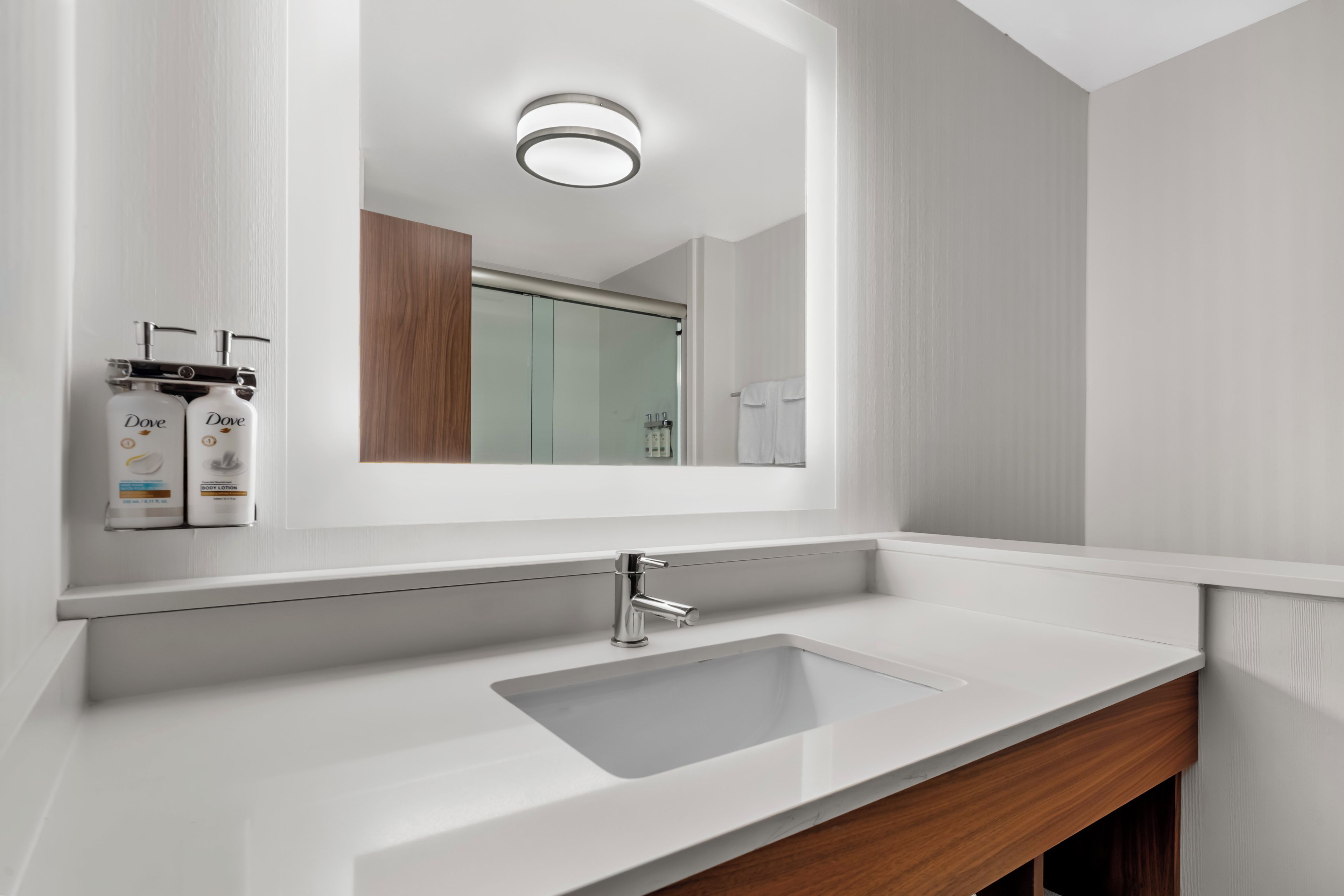 Un baño moderno con un lavabo blanco, un espejo y una ducha que se ve en el reflejo.