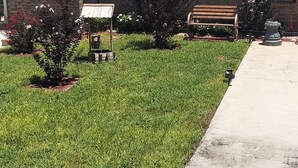A building with a brick facade, a bench, and a small garden area with grass and shrubs. - Gipson Inn Motel (Fort Walton Beach)