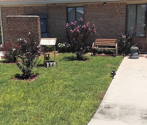 A building with a brick facade, a bench, and a small garden area with grass and shrubs. - Gipson Inn Motel (Fort Walton Beach)
