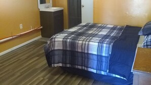 A bedroom with a wooden floor, a bed with a plaid bedspread, a dresser, a mirror, and a wardrobe. - Gipson Inn Motel (Fort Walton Beach)