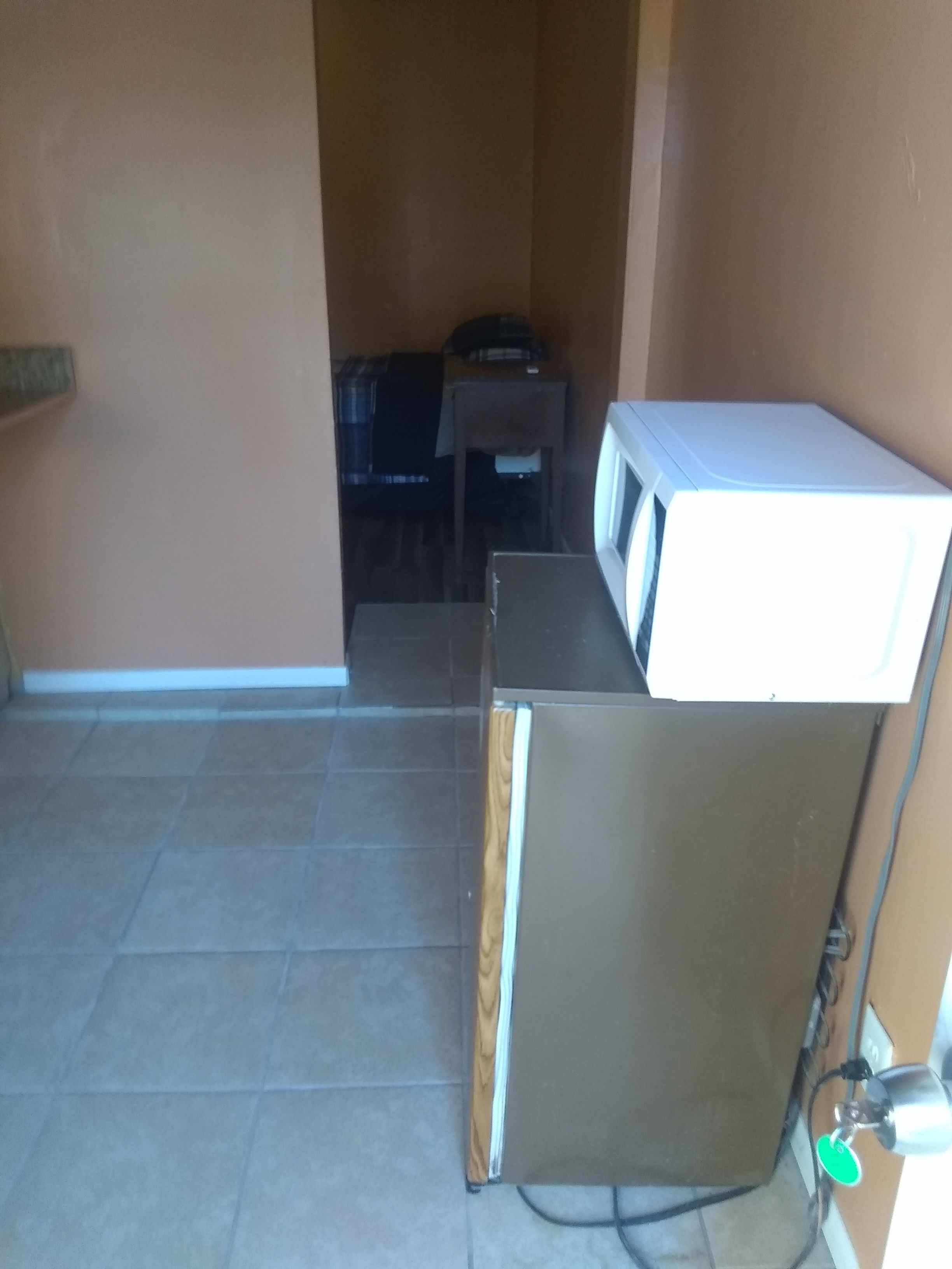 Habitación compacta con refrigerador, microondas y una pequeña mesa con silla.