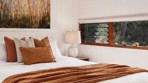 Une chambre à coucher avec un grand lit, des oreillers, une table de chevet avec une lampe et une fenêtre avec des stores.