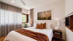 Ein Schlafzimmer mit einem großen Bett, einem Deckenventilator, einem Fenster mit Vorhängen, einem Bild an der Wand und einem Nachttisch mit einer Lampe.