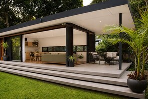 A modern house with an open-plan living area, a kitchen, and a patio with outdoor furniture. - Private Beachfront Bungalow. Pet-Friendly! (Broken Head)