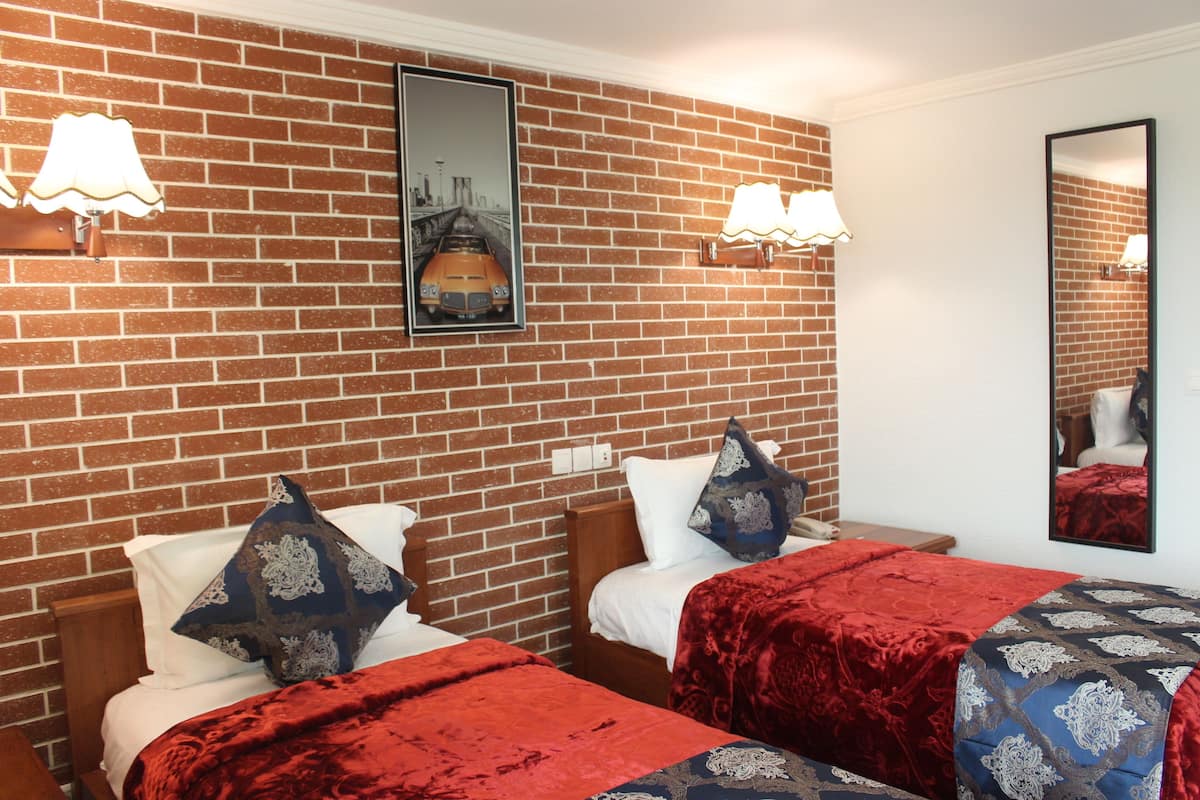 A hotel room with two beds, a brick wall, and a cityscape picture.