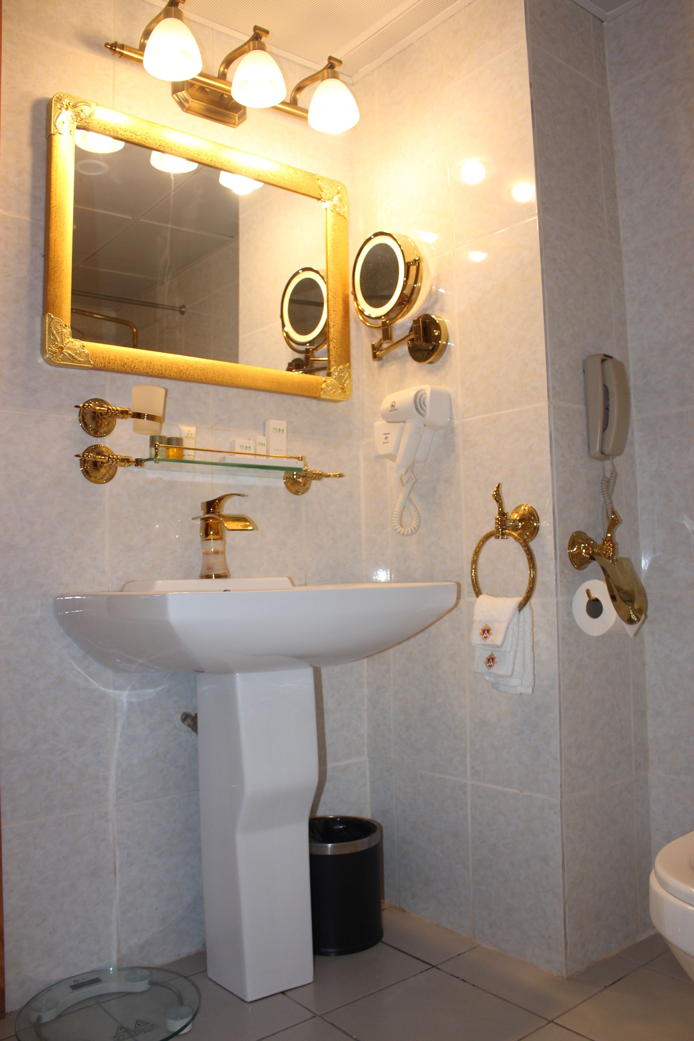 A bathroom with a white sink, gold fixtures, a large mirror, and a toilet.