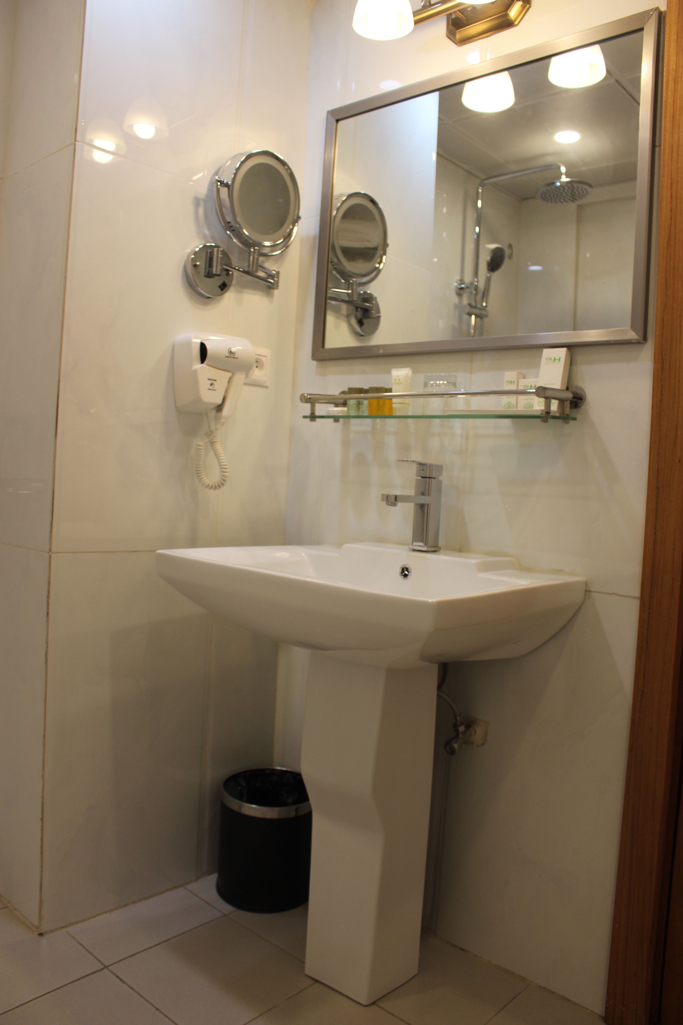A bathroom with a white sink, a mirror, a hairdryer, and a trash can.