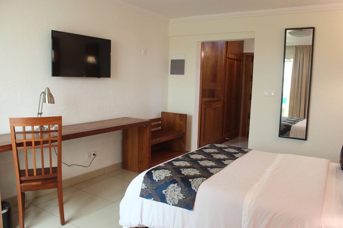 A hotel room with a bed, a desk, a chair, a television, a wardrobe, and a mirror.