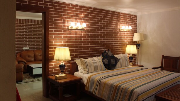 Een hotelkamer met een bakstenen muur, een bed met gestreepte lakens, twee bedlampjes en een nachtkastje met een lamp.