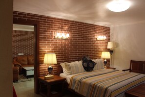 Habitación de hotel con pared de ladrillo, cama con ropa de cama a rayas, dos lámparas de noche y una mesita de noche con lámpara.