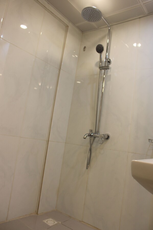 Ducha con cabezal de ducha de mano y grifo empotrado en un baño con azulejos blancos.