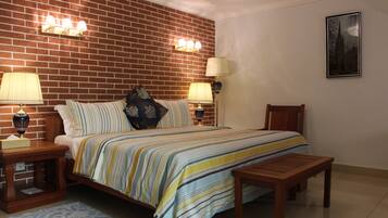 A bedroom with a brick wall, a bed with striped bedding, two bedside lamps, a wooden bench, and a framed picture on the wall.
