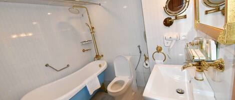 A bathroom with a freestanding bathtub, a toilet, and a sink with gold fixtures.