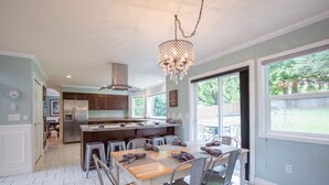 Een moderne keuken met een centraal eiland, roestvrijstalen apparatuur en een eethoek met metalen stoelen.
