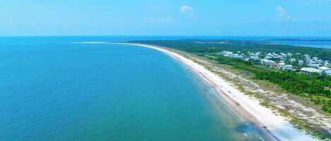 An aerial view of a coastal area with a beach and a residential area with multiple buildings.