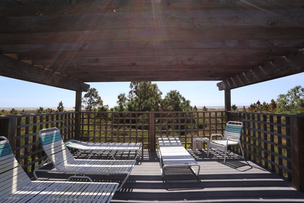 Terraza al aire libre con sillones de descanso y una mesa, rodeada por una valla de madera y árboles.