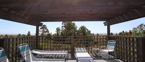 Terraza al aire libre con sillones de descanso y una mesa, rodeada por una valla de madera y árboles.