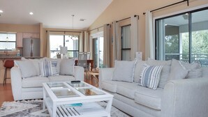 Ein modernes Wohnzimmer mit einer weißen Sofagarnitur, einem Glastisch und einem Deckenventilator.