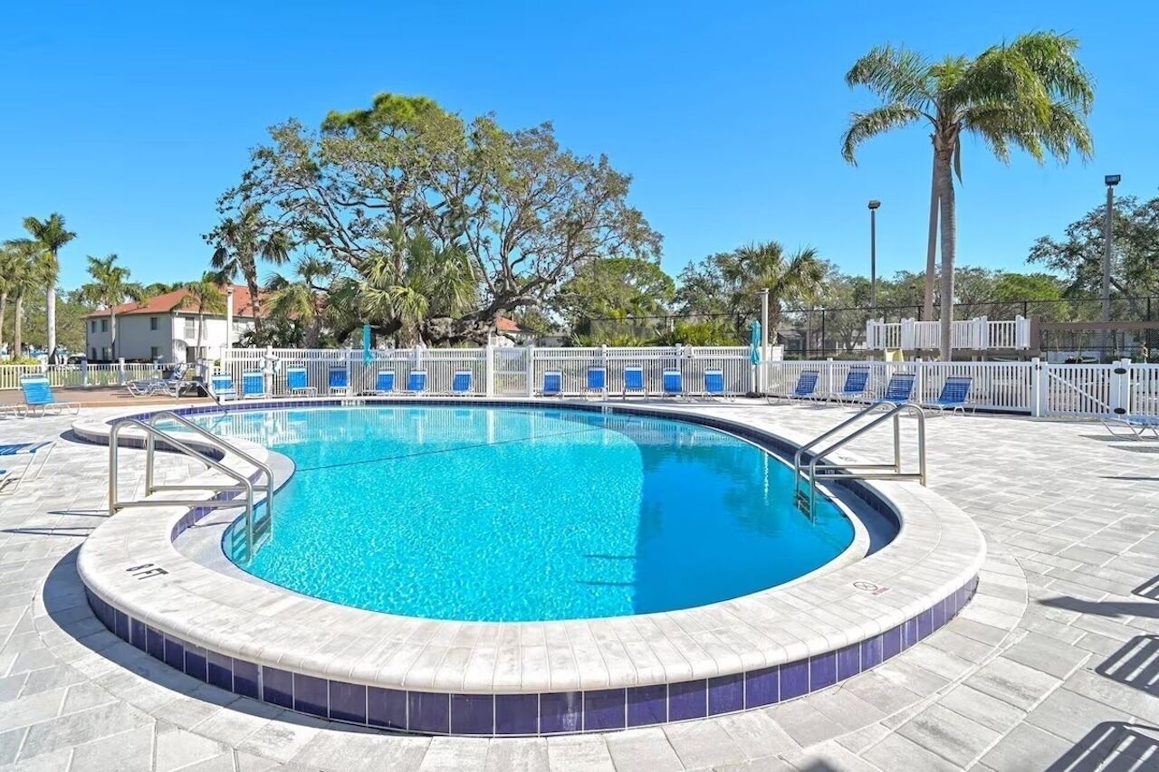 A circular pool with clear blue water, surrounded by a tiled deck and a white fence.
