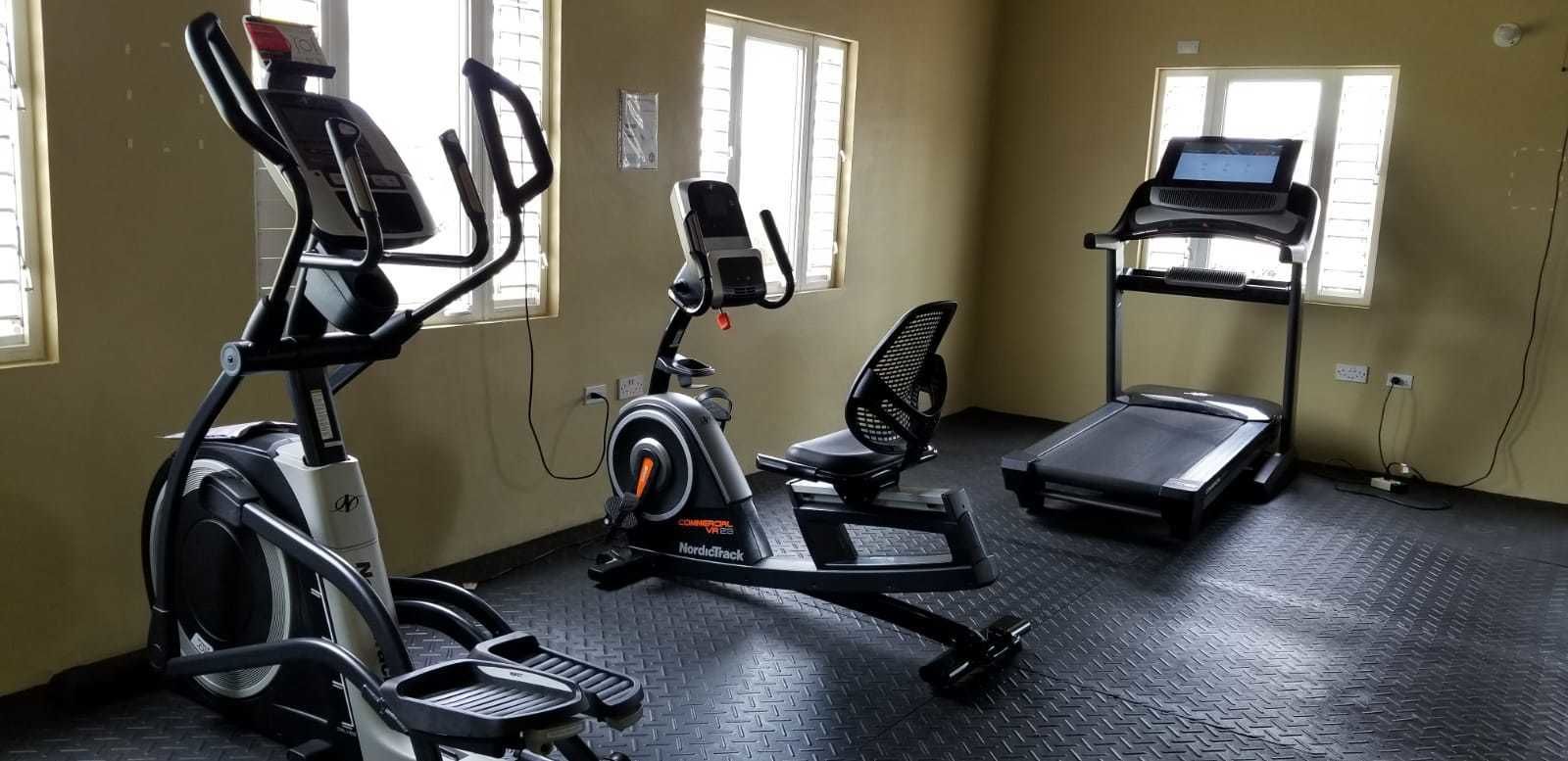 Een fitnessruimte met cardioapparatuur, waaronder een crosstrainer, een hometrainer en een loopband.