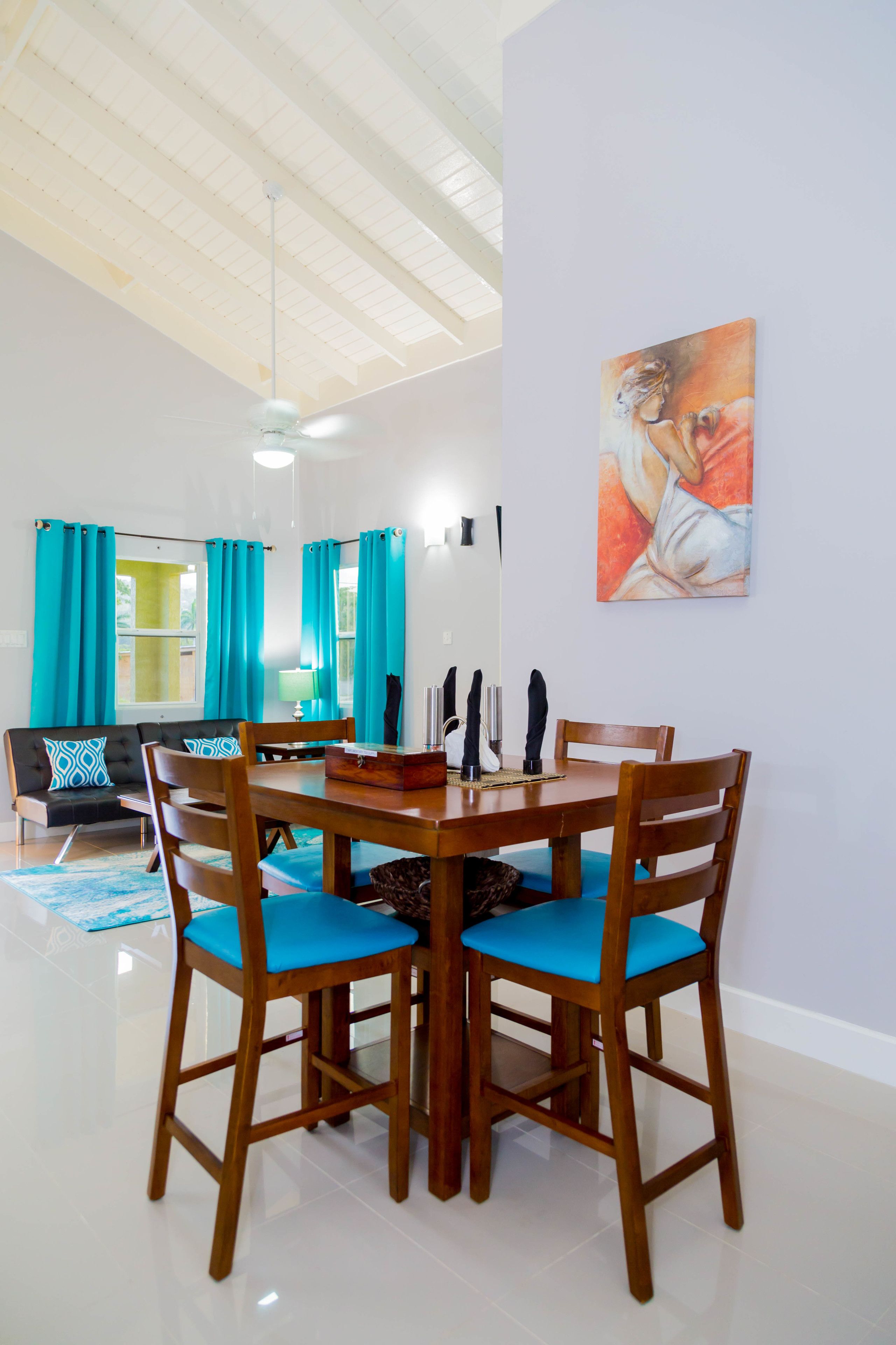 A dining area with a wooden table and chairs, a painting on the wall, and a sofa with patterned cushions.