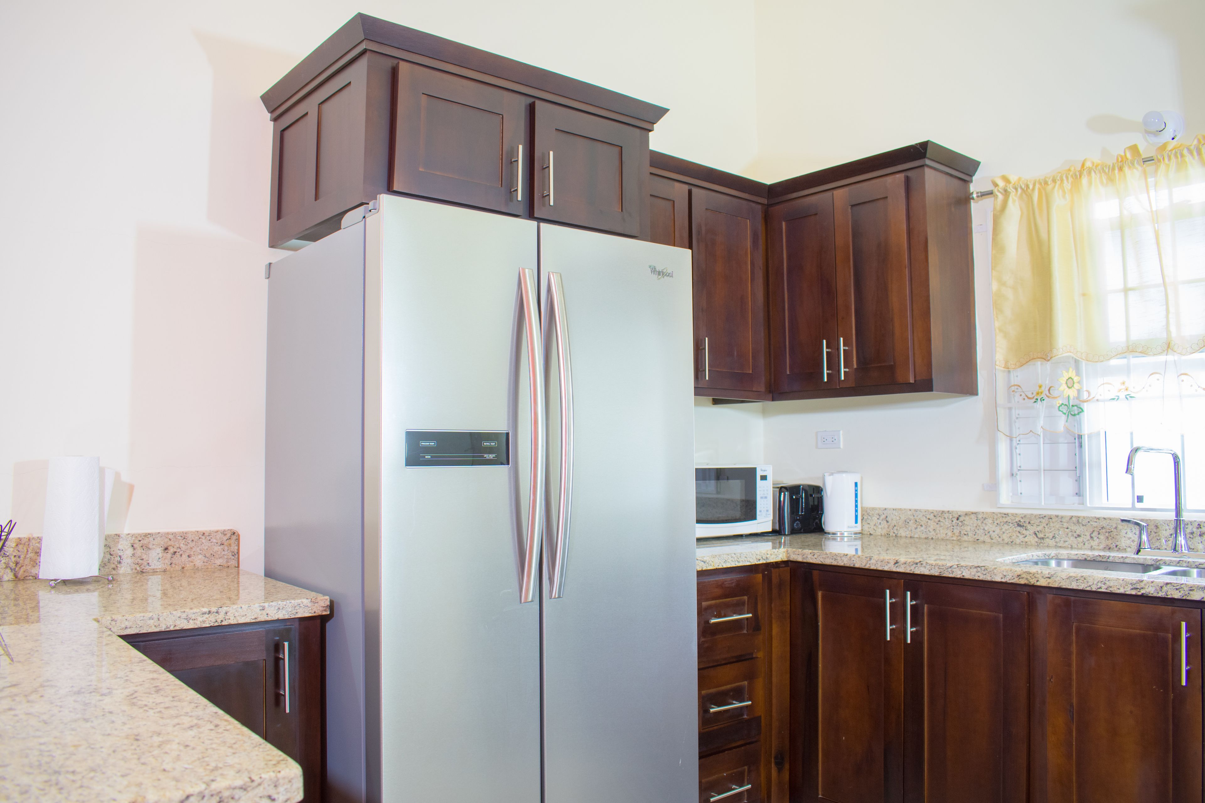 A kitchen with a stainless steel refrigerator, wooden cabinets, a microwave, and a granite countertop.