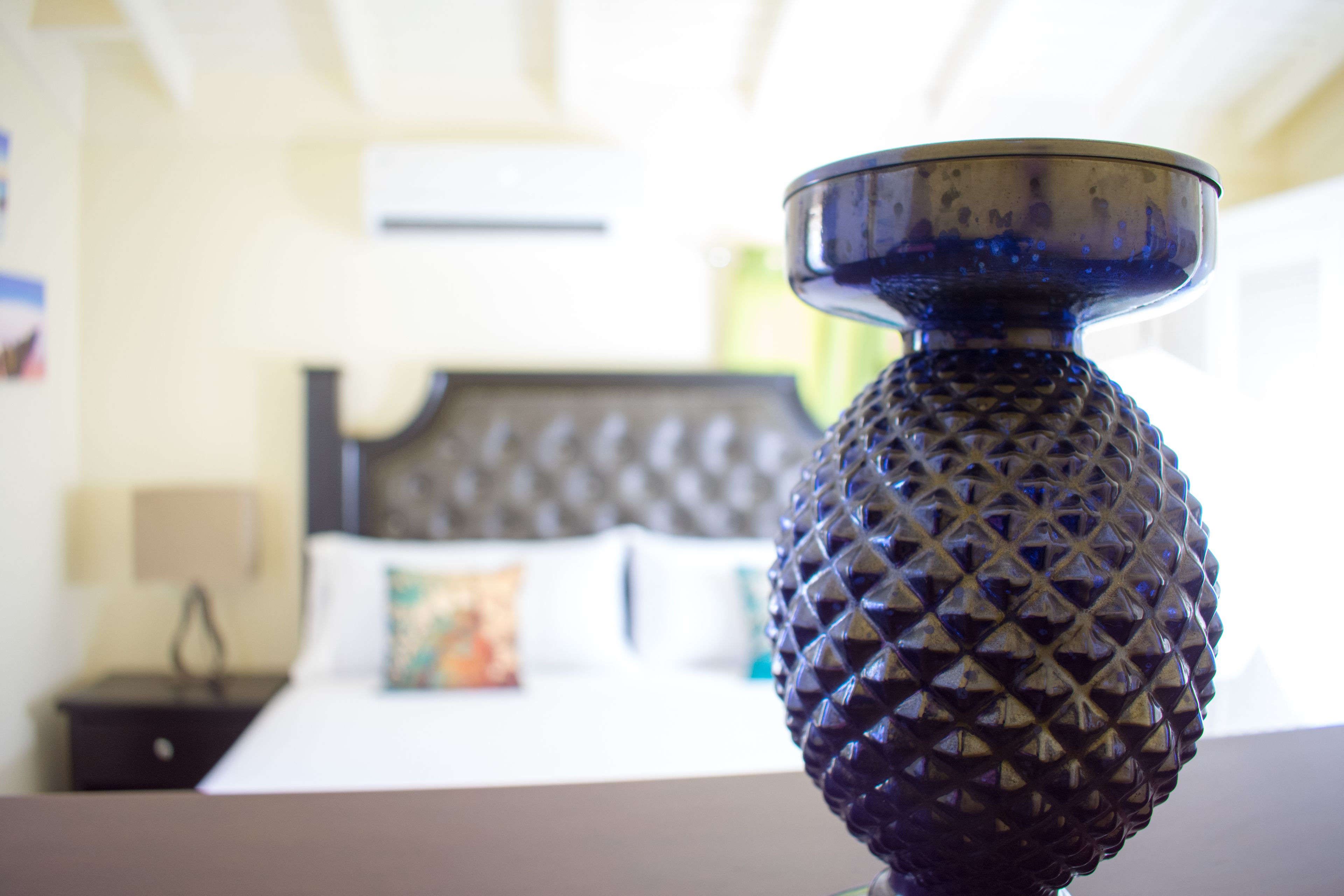 Gros plan d’un vase bleu à la texture particulière, posé sur une table, avec une chambre d’hôtel floue en arrière-plan.
