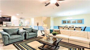 A modern living room with a sofa, armchairs, and a coffee table. There is a dining area with a table and chairs in the background.