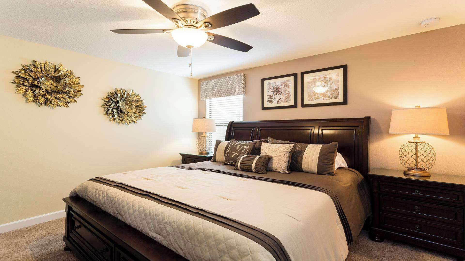 Une chambre à coucher comprenant un lit, un ventilateur de plafond, deux lampes fixées au mur et deux tableaux encadrés.