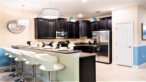 A modern kitchen with dark cabinets, stainless steel appliances, and a central island with bar stools.