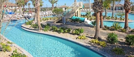 A pool area with clear blue water, palm trees, lounge chairs, and a small slide.