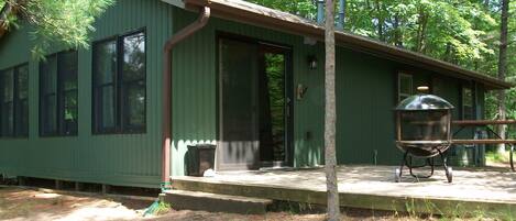 Une cabane verte avec un porche couvert, un barbecue et une porte donnant sur un garage.