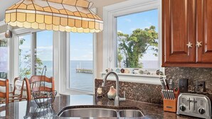 A kitchen with a view of the ocean, a sink, and a window with a starfish decoration.