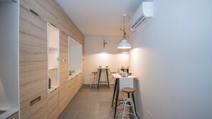 Un couloir étroit avec un lambris en bois sur un des murs, un petit coin cuisine équipé de tabourets et d’une table, et un éclairage suspendu.