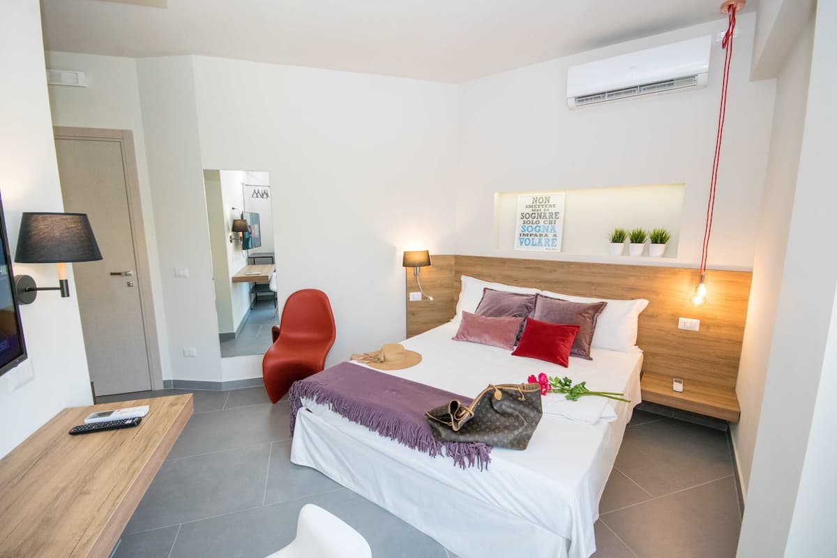 A modern hotel room with a bed, bedside table, lamp, and a small desk with a remote control.