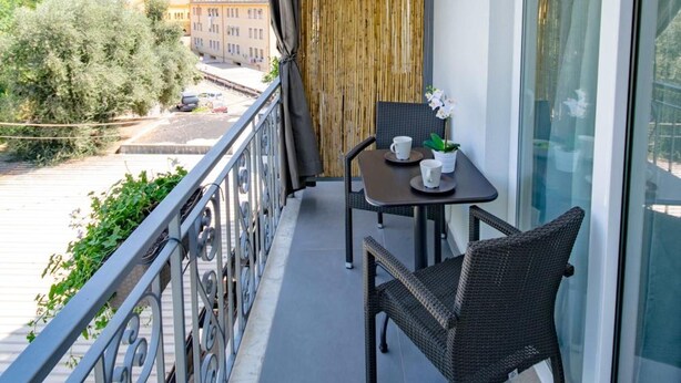 Un balcon avec une table et des chaises, une vue sur les bâtiments et les montagnes, et une balustrade.