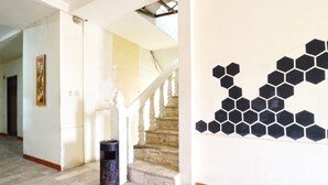 A hallway with a staircase, a trash bin, and a wall with hexagonal tiles. - Wisma Gading Indah (Jakarta)