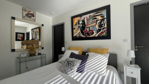 A modern bedroom with a large bed, a bedside table, a lamp, and a wall-mounted painting. - Domaine Georges V (Saint-Junien)