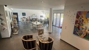 A spacious dining area with a large table and chairs, a decorative wall with artwork, and a view of the outdoors through large windows. - Domaine Georges V (Saint-Junien)
